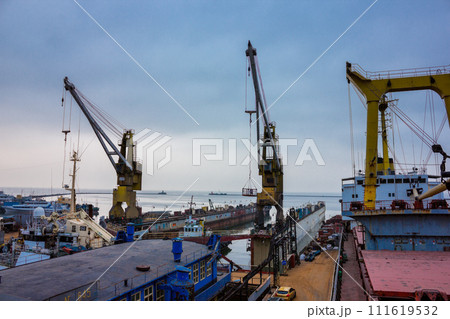 Industrial floating dock in a shipyard, cranes towering above. Vessel under repair, maritime equipment visible. Overcast sky suggesting outdoor labor in a coastal ship repair yard. 111619532