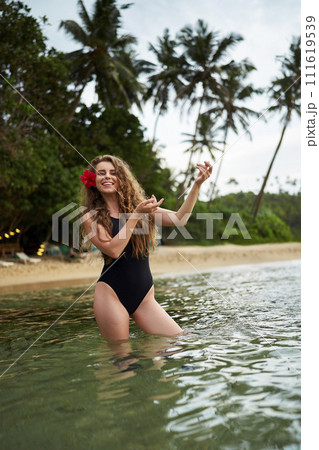 Woman in swimsuit performs hula dance in sea, flower in hair. Tropical beach backdrop, palm trees. Solo traveler enjoys Hawaiian culture, summer vibes. Leisure, tradition blend on sunny coast. Woman in swimsuit performs hula dance in sea, flower in hair. Tropical beach backdrop, palm trees. Solo traveler enjoys Hawaiian culture, summer vibes. Leisure, tradition blend on sunny coast. 111619539