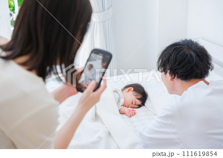 昼寝する赤ちゃんの写真を撮る夫婦 111619854