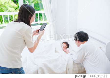 昼寝する赤ちゃんの写真を撮る夫婦 昼寝する赤ちゃんの写真を撮る夫婦 111619855