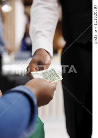 Close up of male African American waiter receiving tip from generous hotel guest. Tourist giving money cash to restaurant worker, making order, paying bill. Tipping in hospitality industry Close up of male African American waiter receiving tip from generous hotel guest. Tourist giving money cash to restaurant worker, making order, paying bill. Tipping in hospitality industry 111620397