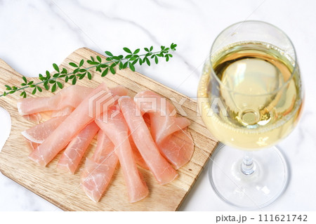 塩味が効いておいしい生ハムをおつまみに、辛口の白ワインを飲む 111621742