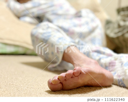 畳んだ布団の上に倒れている寝間着姿の高齢女性の足の裏 111622340