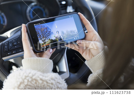 運転席でジャグリング動画を見る若い女性手元 111623738