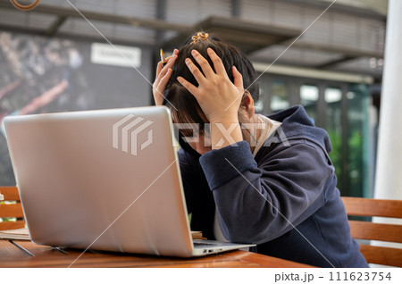 A stressed young Asian woman is feeling overworked and tired while working remotely at a cafe. 111623754