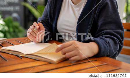 A cropped shot of a woman writing down her ideas in a book while sitting in a cafe. 111623761