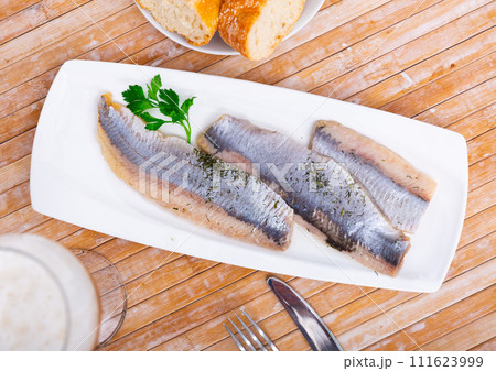 On table is plate with appetizer –salted Atlantic herring fillet decorated with parsley 111623999