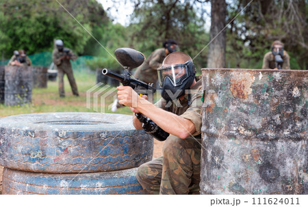 Paintball player in camouflage and mask aiming with gun in shootout Paintball player in camouflage and mask aiming with gun in shootout 111624011