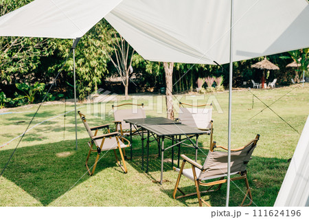 Set up your outdoor picnic with a summer camping tent, tables, and chairs. This suburban patio offers a perfect shade and relaxation spot with comfortable seating for a nature-filled celebration. 111624196