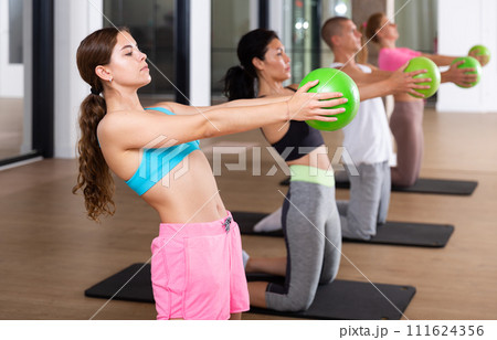 Sports people perform an exercise holding a mini Pilates ball in front of them 111624356