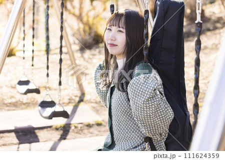 公園のブランコに座って景色を眺めるギターを背負った女性 公園のブランコに座って景色を眺めるギターを背負った女性 111624359