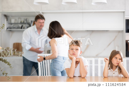 Family problem, conflict and people concept - sad children sitting at table their parents quarreling at home Family problem, conflict and people concept - sad children sitting at table their parents quarreling at home 111624584