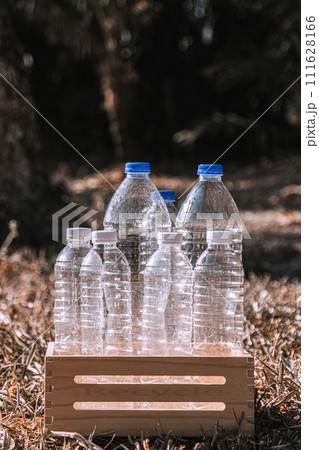 Vertical Photo Several plastic water bottles are placed in a wooden crate for recycling on dry grass in a natural forest. 111628166