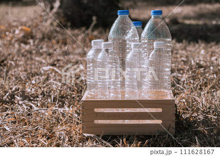 Horizontal Photo Several plastic water bottles are placed in a wooden crate for recycling on dry grass in a natural forest. Horizontal Photo Several plastic water bottles are placed in a wooden crate for recycling on dry grass in a natural forest. 111628167