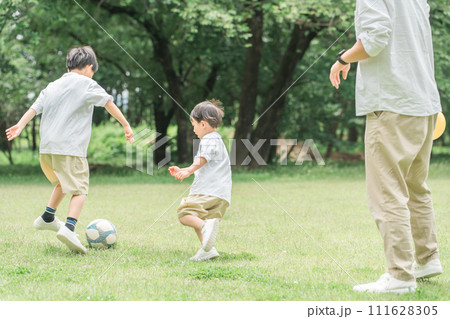公園の芝生でサッカーをする兄弟・友達・男の子・親子・父親（サッカーボール・ドリブル） 111628305