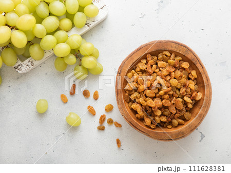 Green sweet dried raisins in wooden bowl on light background with ripe grapes. Green sweet dried raisins in wooden bowl on light background with ripe grapes. 111628381