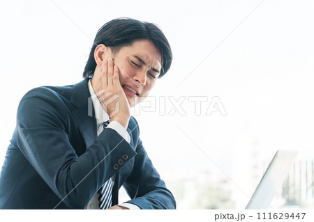 虫歯・顎の痛みで悩むデスクワークをしている若いアジア人男性ビジネスマン 111629447
