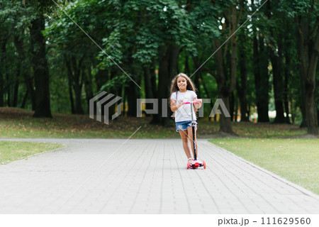 Little girl riding a scooter at the park in summer 111629560