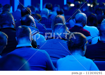 Audience at conference event listening to speaker in blue lit room 111630291