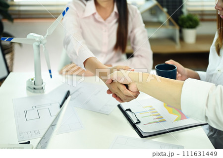 Businesswoman and engineer shaking hands over meeting table. Green energy development concept Businesswoman and engineer shaking hands over meeting table. Green energy development concept 111631449