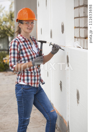 Insulation of the house with polyfoam. The worker is checking with the construction level the accuracy of the installation of polystyrene board on the facade. Insulation of the house with polyfoam. The worker is checking with the construction level the accuracy of the installation of polystyrene board on the facade. 111633698