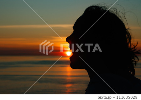 Girl silhouette with open mouth in magical sunset over the Gulf of Finland, Baltic sea. Girl silhouette with open mouth in magical sunset over the Gulf of Finland, Baltic sea. 111635029