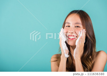 Portrait beautiful female smile applies foaming cleanser healthy skin, Asian women face wash exfoliating scrub soap with skincare cleansing, Studio isolated on blue background, skincare daily routine 111636380
