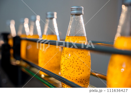 Quality manufacturing in the bottling factory is visible as transparent bottles are filled with basil or chia seed drinks infused with pomegranate. This automated process ensures a healthy outcome. 111636427
