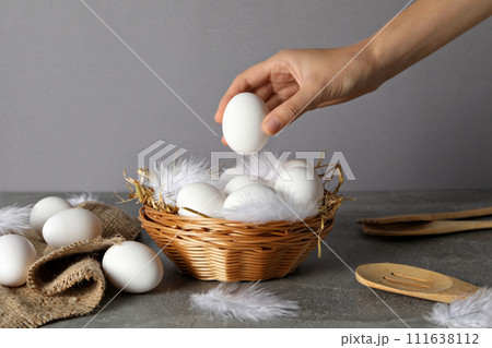Eggs in a wicker basket, with a hand, on a gray background. 111638112