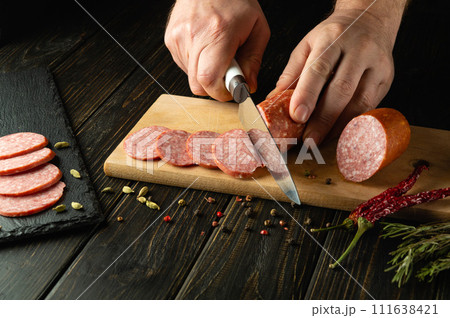 Slicing salami sausage with a knife in the hand of a chef for serving a festive table in a restaurant 111638421