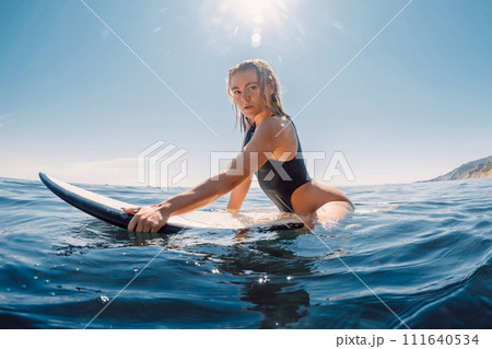 Young surfer woman on surfboard in blue ocean. Blonde sexy surfer girl with sporty body Young surfer woman on surfboard in blue ocean. Blonde sexy surfer girl with sporty body 111640534