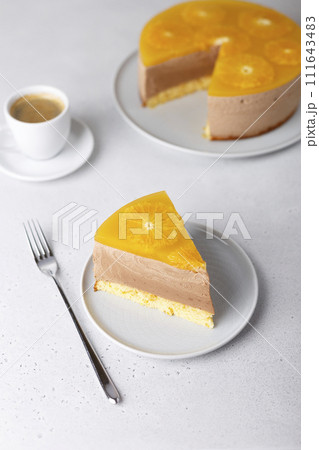 Chocolate-orange mousse cake with biscuit base, jelly and orange circles. Piece of homemade cheesecake and a cup of coffee. Traditional holiday dessert. Selective focus, close-up. Chocolate-orange mousse cake with biscuit base, jelly and orange circles. Piece of homemade cheesecake and a cup of coffee. Traditional holiday dessert. Selective focus, close-up. 111643483