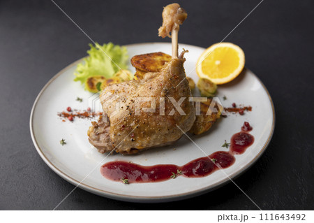 Duck leg confit with Brussels sprouts, baked potatoes, thyme, orange and lingonberry sauce. Traditional French cuisine. Selective focus, close-up, black background. 111643492