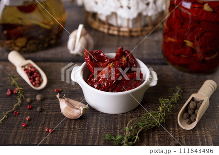 Sun-dried tomatoes in olive oil in a white bowl with pepper, garlic and thyme in a rustic style. Selective focus, close-up. Sun-dried tomatoes in olive oil in a white bowl with pepper, garlic and thyme in a rustic style. Selective focus, close-up. 111643496