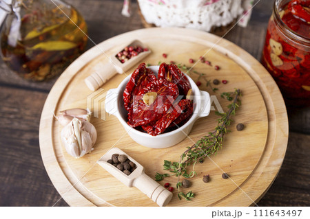Sun-dried tomatoes in olive oil in a white bowl with pepper, garlic and thyme on a wooden board. Home cooking, rustic style. Selective focus, close-up. 111643497