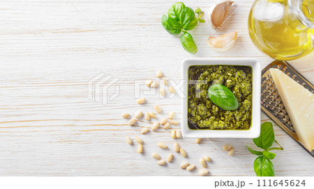 Homemade pesto sauce in small square jar and ingredients for pasta on white wooden background Homemade pesto sauce in small square jar and ingredients for pasta on white wooden background 111645624