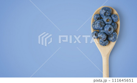 Fresh organic blueberries in wooden spoon isolated on blue background with copy space 111645651