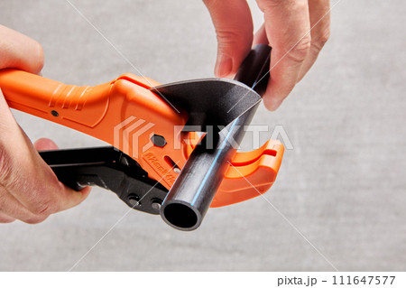 Using pipe cutter with ratcheting mechanism when installing sprinkler water line, close-up of cutting plastic pipe. 111647577