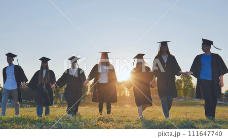Graduate students walking through an evening meadow at sunset. Graduate students walking through an evening meadow at sunset. 111647740