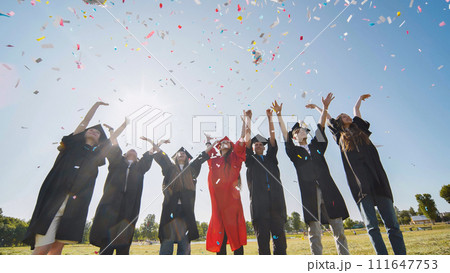 Happy college graduates throw colorful confetti against the rays of sunshine. 111647753