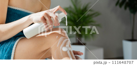 Anonymous woman pushing pump plastic soap bottle, using foam gel pump dispenser in bathroom. Close up view of female applying body lotion on leg during morning shower. Skin care, routine concept. Anonymous woman pushing pump plastic soap bottle, using foam gel pump dispenser in bathroom. Close up view of female applying body lotion on leg during morning shower. Skin care, routine concept. 111648707