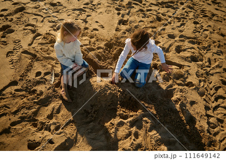 Two little girls, sister sitting on the beach and building a sand castle. Concept of the family vacation. Two little girls, sister sitting on the beach and building a sand castle. Concept of the family vacation. 111649142