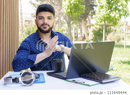 Front view of stylish young businessman working outdoors. Handsome asain guy sitting at table, using laptop, looking at camera, rubbing hands. Concept of urban lifestyle. 111649444