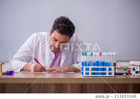 Young male chemistry teacher sitting in the classroom Young male chemistry teacher sitting in the classroom 111653348