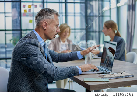 Confident businessman sitting at conference table in modern office Confident businessman sitting at conference table in modern office 111653562