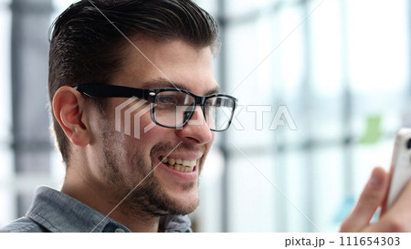 A man's face is in close-up with glasses, he uses a phone 111654303