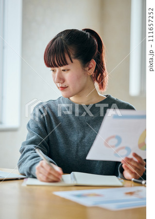 資料を持ちノートにメモをする若い女性 資料を持ちノートにメモをする若い女性 111657252