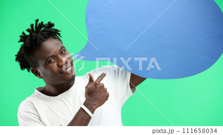 A man, close-up, on a green background, shows a blue comment sign 111658034