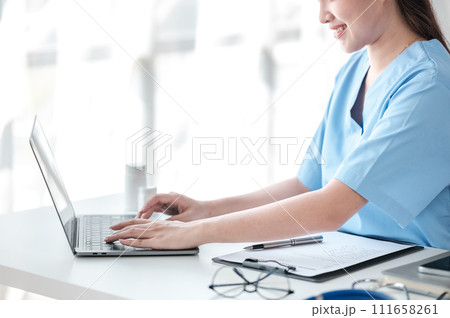 Asian female doctor working on laptop, filling out paperwork, patient medical history, reviewing documents at her workplace medical and health concept Asian female doctor working on laptop, filling out paperwork, patient medical history, reviewing documents at her workplace medical and health concept 111658261