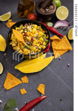Freshly made mango salsa in a black ceramic bowl, nacho chips and ingredients Freshly made mango salsa in a black ceramic bowl, nacho chips and ingredients 111658882